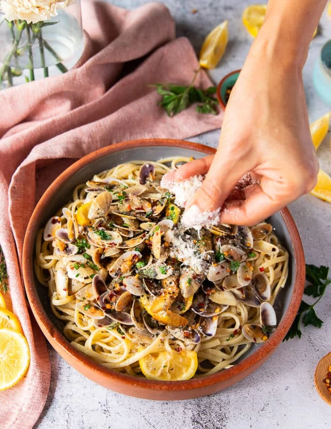 A hand adding the pasta and some parmesan sprinkle optionally