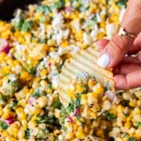 close up of a hand using tortilla chips to scoop up some mexican street corn salad