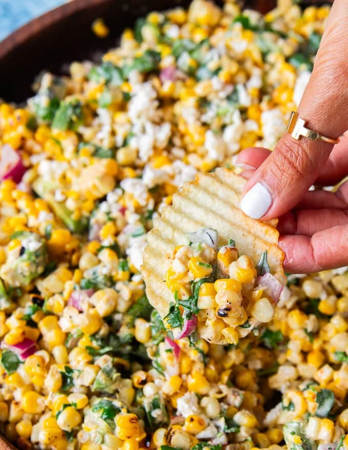 close up of a hand using tortilla chips to scoop up some mexican street corn salad