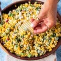 A hand holding a chips and scooping some mexican corn salad with creamy cilantro lime dressing, jalapenos and avocados