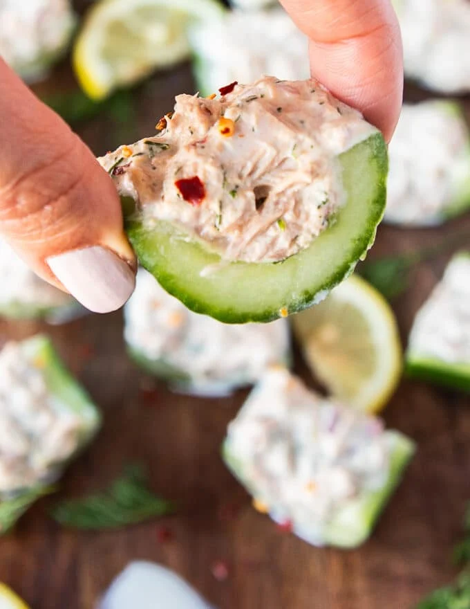 A hand holding a piece of cucumber topped with tuna salad for the best bites of tuna cucumber salad