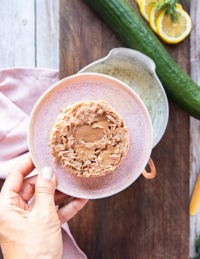 drained canned tuna in a plate and a hand holding it