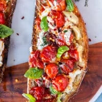 one whole caprese toast close up showing the sourdough toast, the ripe sweet baby tomatoes, mozzarella, garlic, basil leaves and chilli flakes drizzled with olive oil