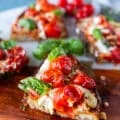 close up of a cut up caprese toast showing the blistered tomatoes, mozzarella and basil leaves drizzled with some olive oil and light balsamic syrup