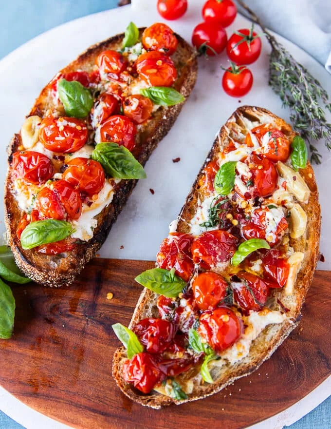 caprese toast on a marble with the tomato mixture and mozzarella and basil spread over it