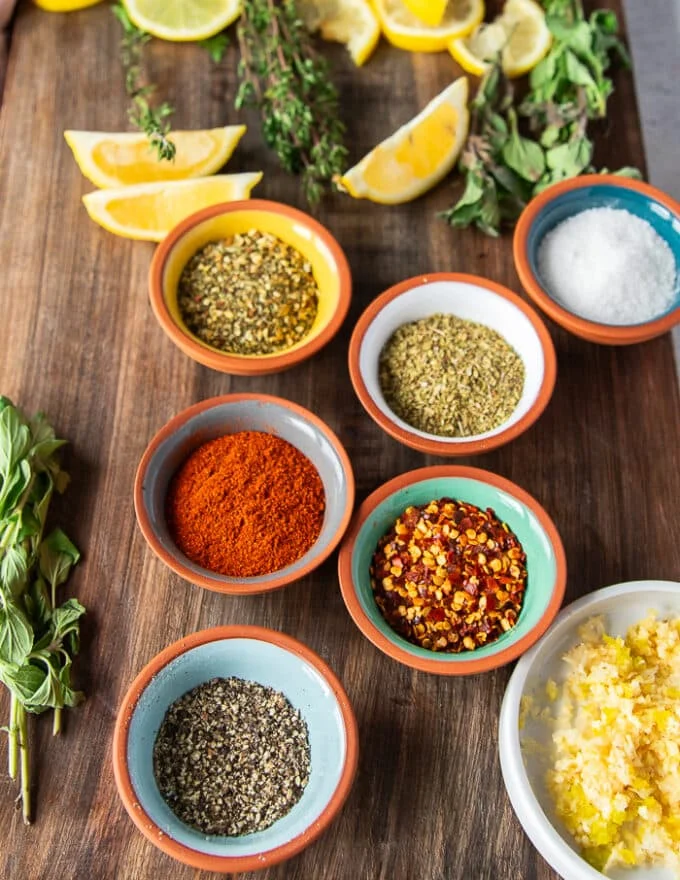 Ingredients to make crawfish tail including the crawfish tails peeled and ready, some garlic, butter, olive oil in bowls, spices in a bowl and lemon zest, some fresh herbs