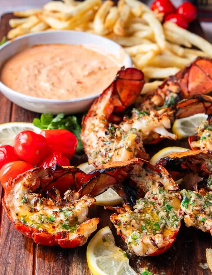 side view of grilled lobster with melted butter and herbs on a wooden board
