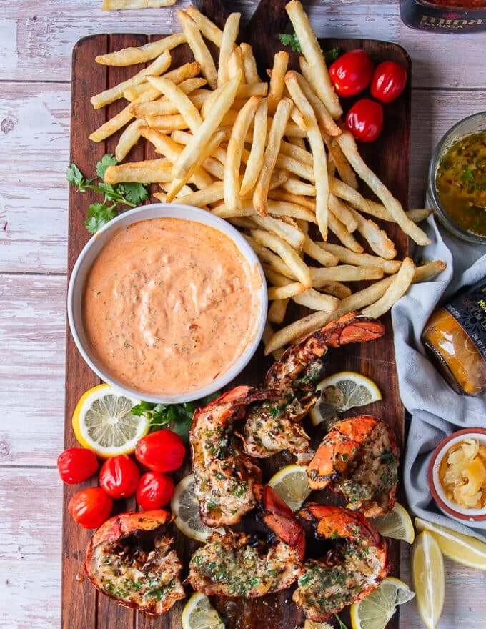 full platter of grilled lobster, fries, some harissa aioli, lemon wedges and baby tomatoes on the side