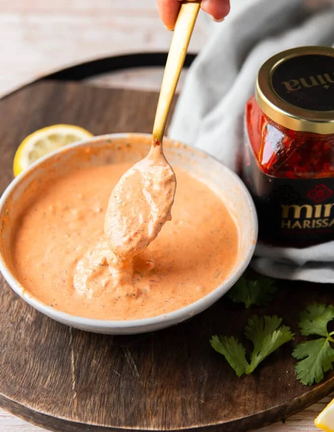 A spoon mixing the ingredients together and showing a perfect drip of harissa aioli from the bowl