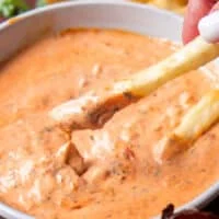 close up of a french fry dipped into harissa aioli and the sauce dripping off the fries