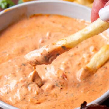 close up of a french fry dipped into harissa aioli and the sauce dripping off the fries