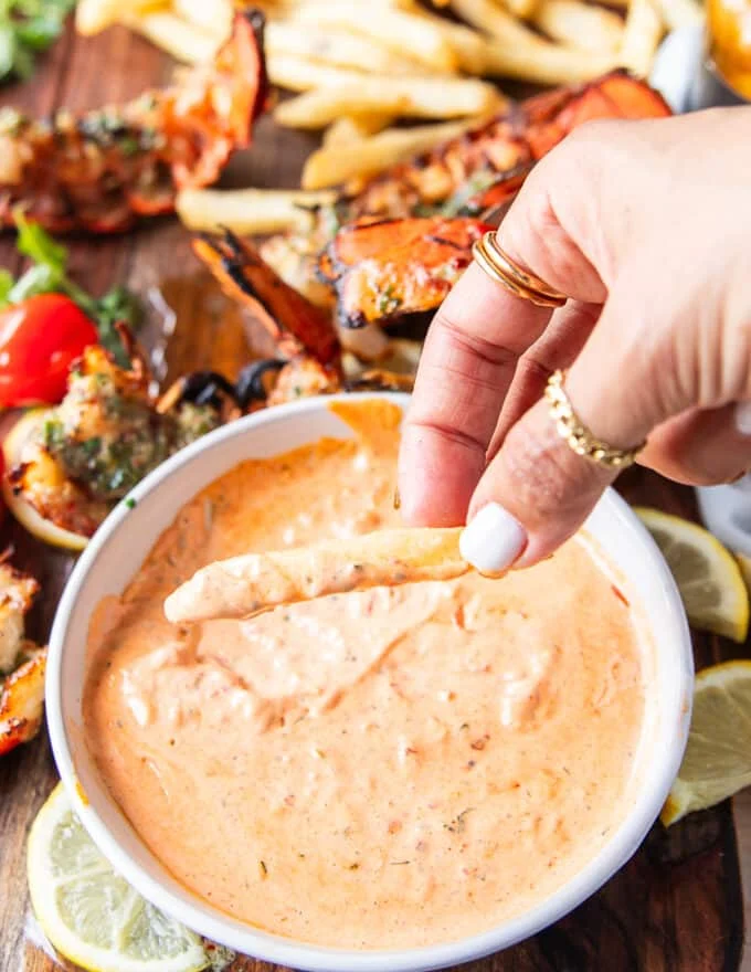 Fries dipped in harissa aioli and showing close up of the sauce dripping