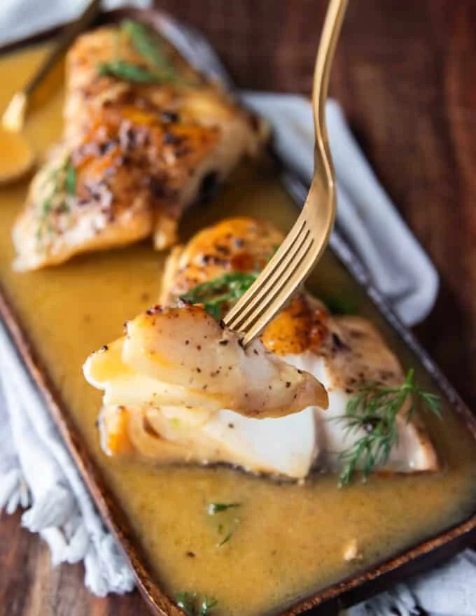 A fork holding a piece of fish drenched in lemon garlic butter sauce