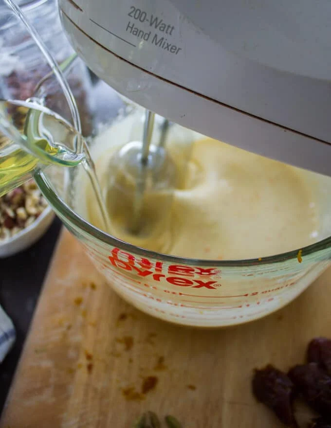 A hand pouring the oil into the bowl of eggs and sugar