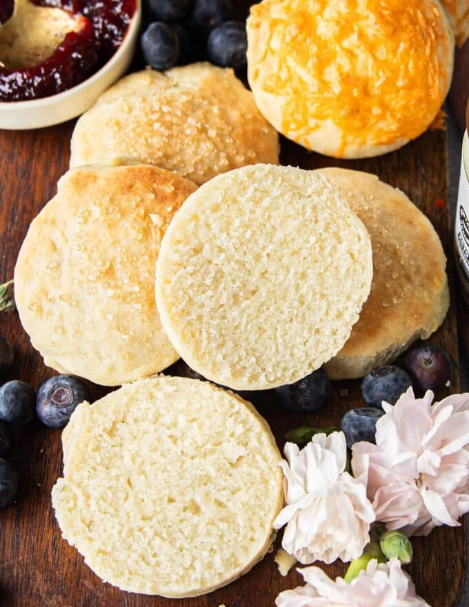 A mayonnaise biscuit split in half showing the fluffy texture on the inside on a plate with other biscuits