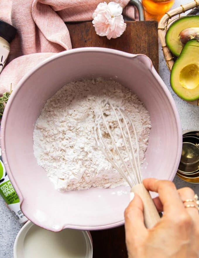 A hand whisking the flour, salt and baking powder in a large bowl to make the dough