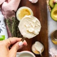 A hand holding a half cup measuring c up with mayonnaise