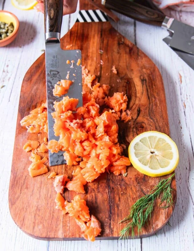 A knife dicing the fresh salmon fillet on a board to make salmon patties