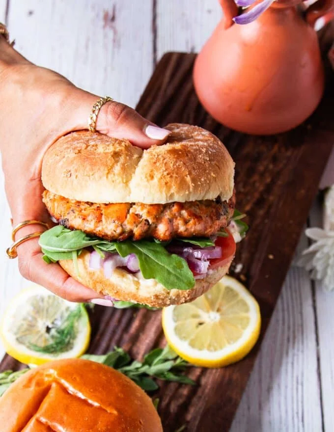 A hand holding salmon burgers assembled and ready