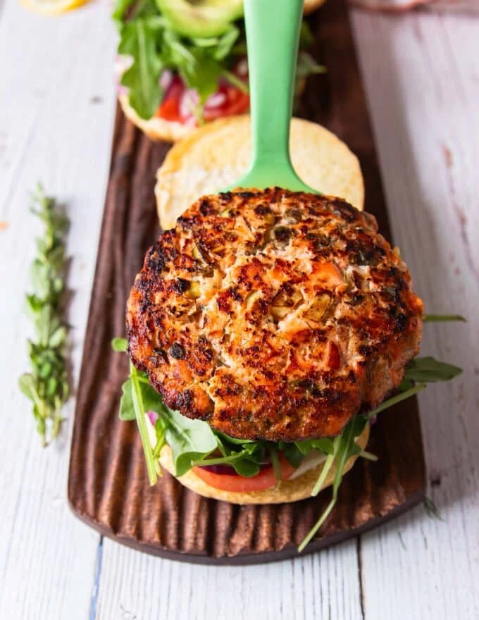 The golden perfectly cooked salmon burger going on to the bun to make the burger somplete