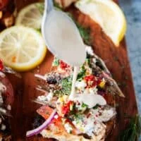 A spoon drizzling a hefty amount of tahini sauce over the sardines on toast