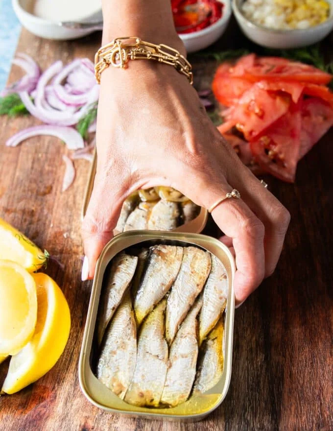 A hand holding a can of sardines opened up showing the sardines in olive oil in a tin