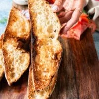 A hand holding toasted crunchy sourdough toasted slices to make sardines on toast