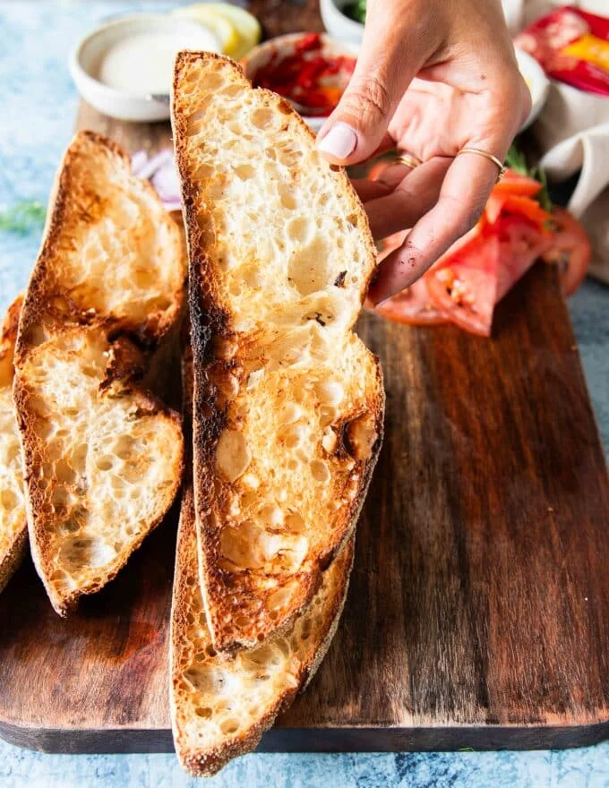 A hand holding toasted crunchy sourdough toasted slices to make sardines on toast