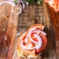 tomato slices and onion slices are layered over the tasted bread