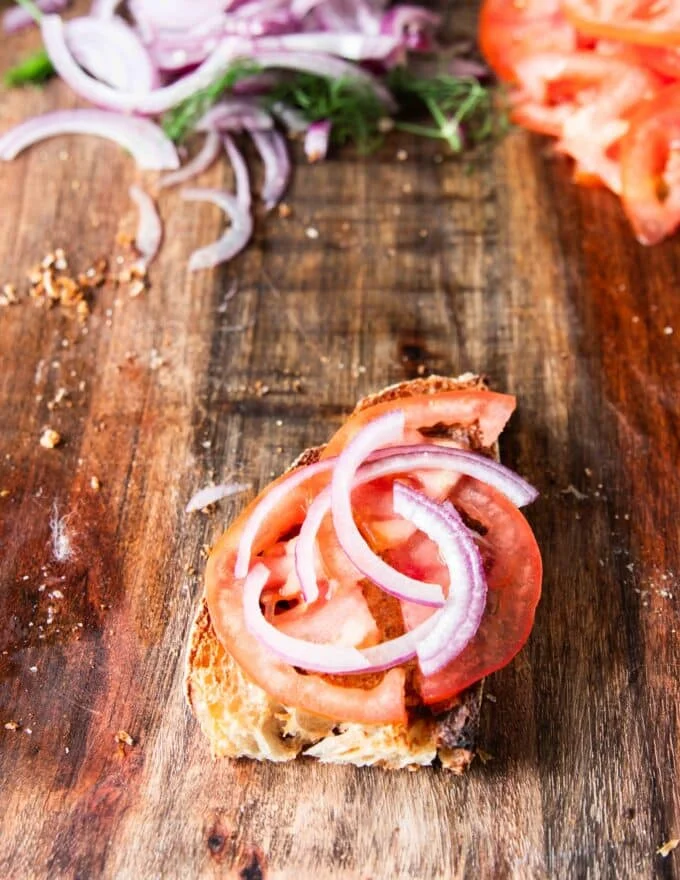 tomato slices and onion slices are layered over the tasted bread