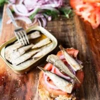 4 pieces of baby sardines from the can are placed over the tomatoes and onions on the toast to layer the toast recipe