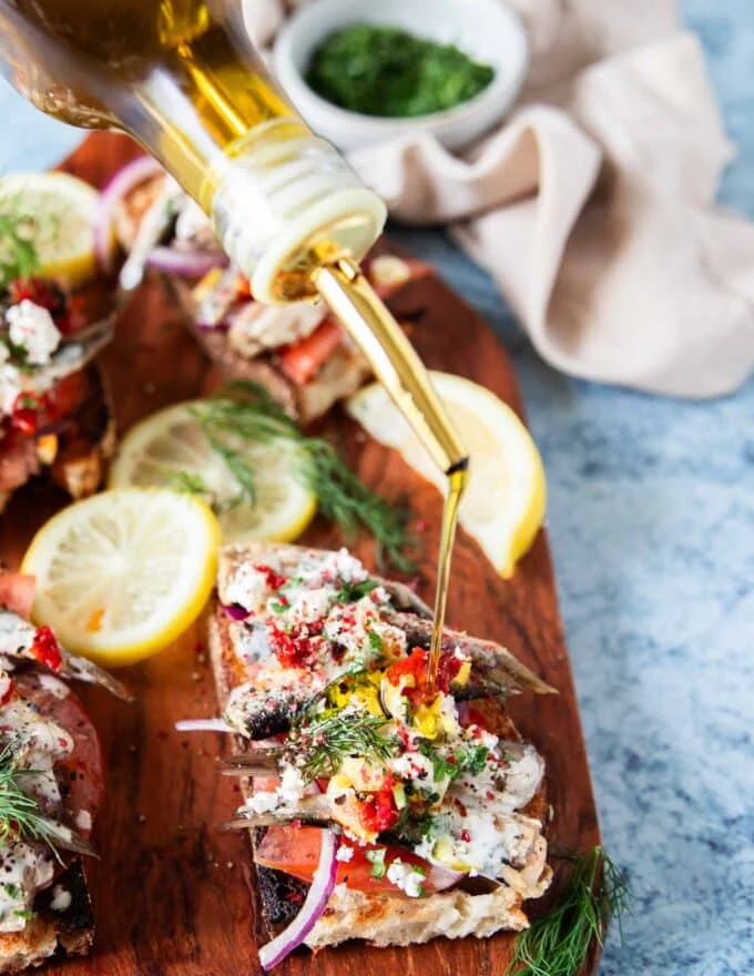 A bottle drizzling some olive oil over the sardines on toast to finish the recipe
