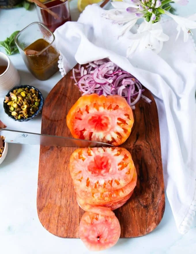 Making the tomato carpaccio recipe: A hand slicing the heirloom tomatoes using a sharp knife on a board