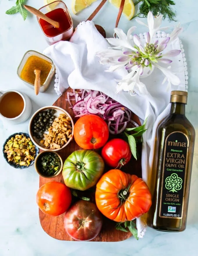 Tomato Carpaccio Ingredients on a board, heirloom tomatoes, olive oil capers, seasoning, olives and pistachios