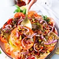A hand holding a serving spoon and serving the finished tomato carpaccio