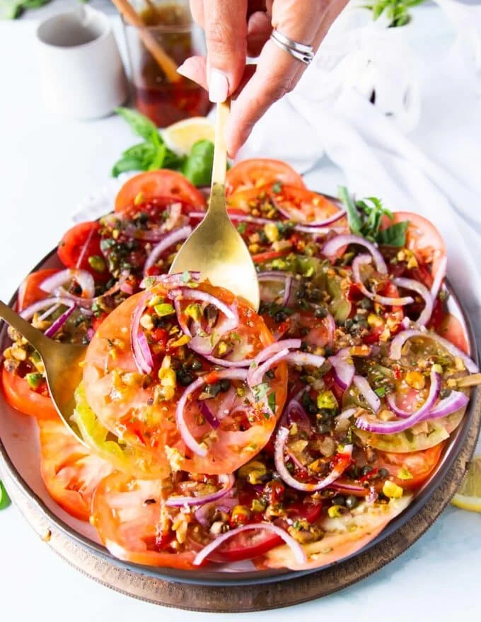 A hand holding a serving spoon and serving the finished tomato carpaccio
