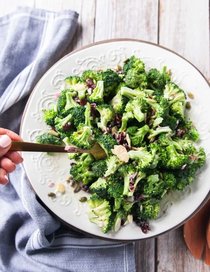 Broccoli salad with creamy dressing on a plate and a hand scooping it