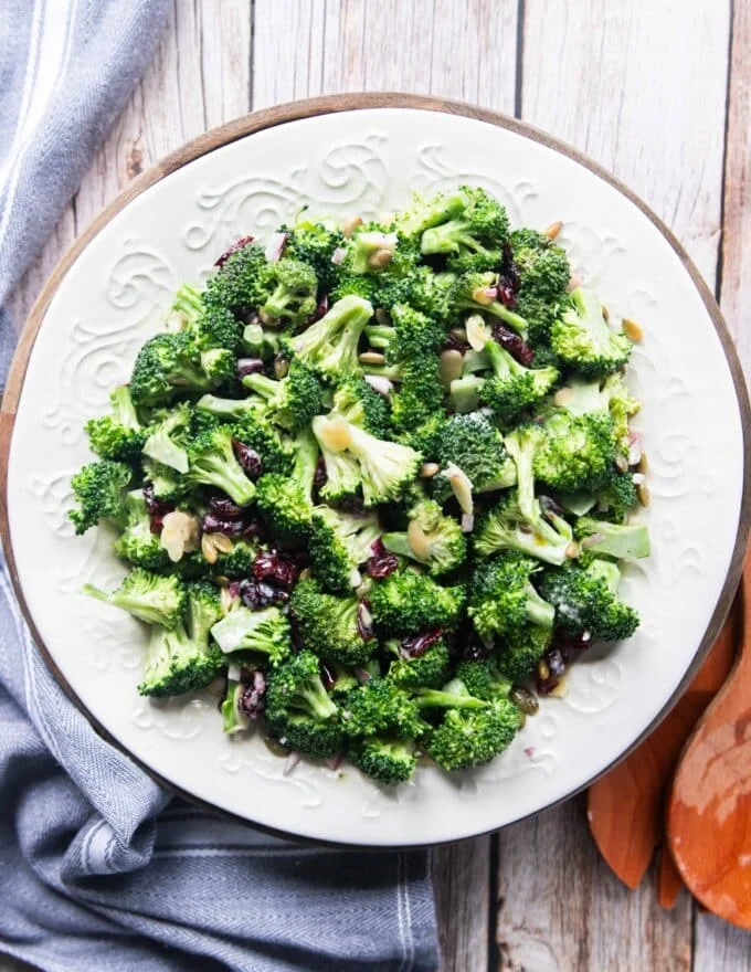 Creamy broccoli salad on a white plate with cranberries, sunflower seeds and onions