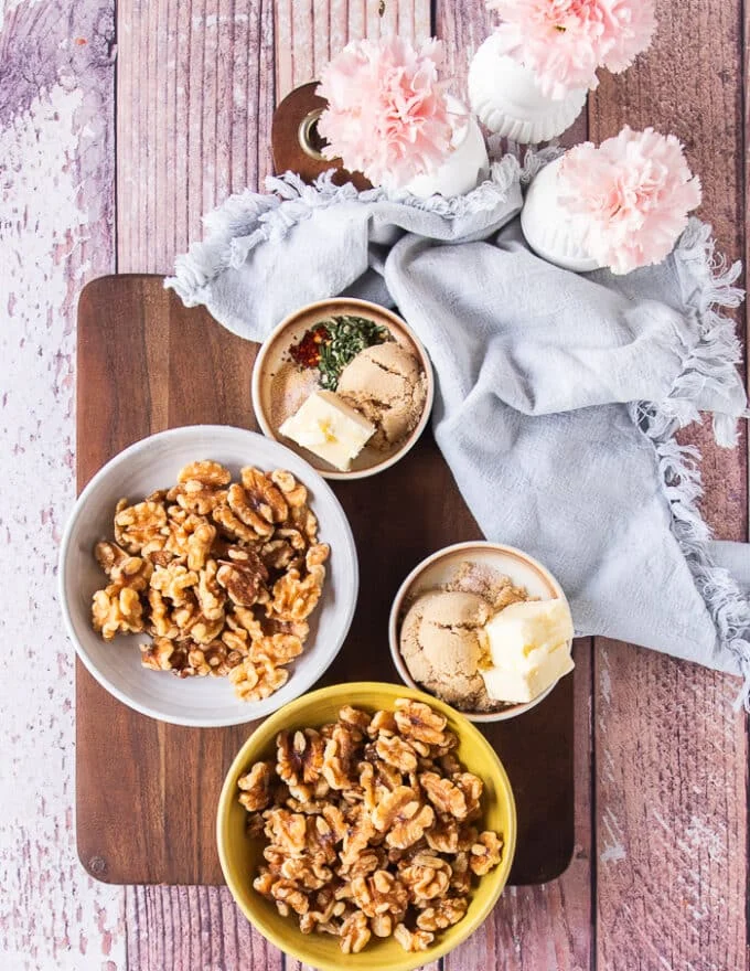 Ingredients to make candied walnuts on a board including walnuts, brown sugar, butter and a variation with spices and rosemary
