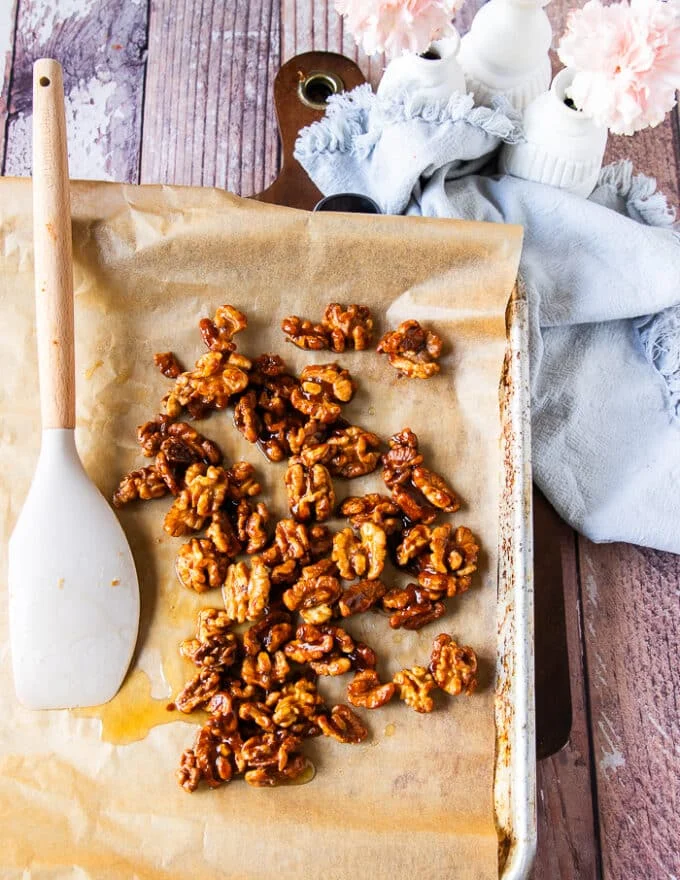 Walnuts spread on parchment paper in a baking sheet to cool down