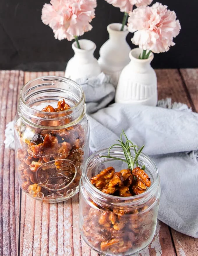 2 jars of glossy candied walnuts on a table with a tea towel