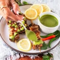 A hand drizzling chermoula sauce over halibut
