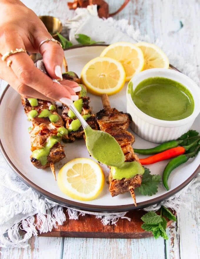 A hand drizzling chermoula sauce over halibut