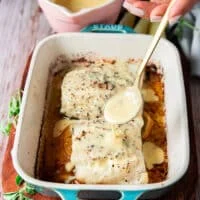 a hand drizzling some citrus beurre blanc over the baked chilean sea bass