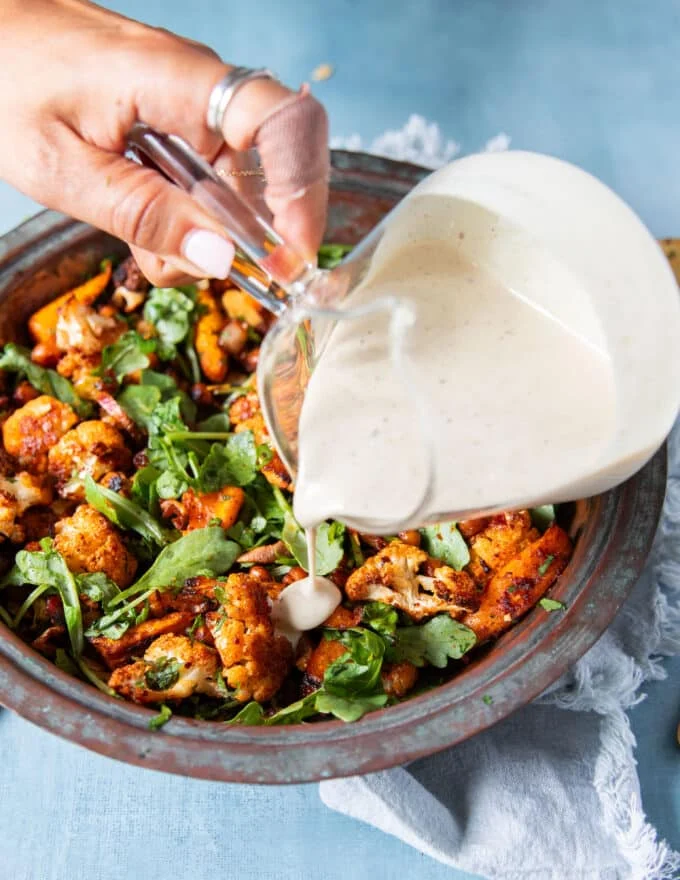 Tahini sauce is generously being poured over the cauliflower salad