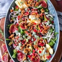 salad ingredients are piled together including arugula fresh figs, nuts, blue cheese, red onions, apples and avoocado