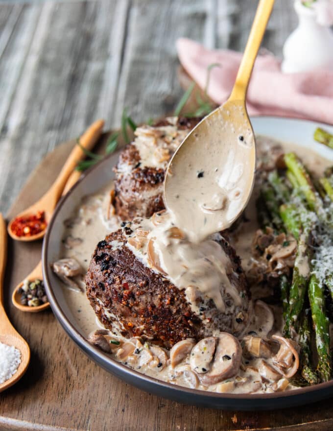 A hand spooning generous amount of mushroom sauce over the steak