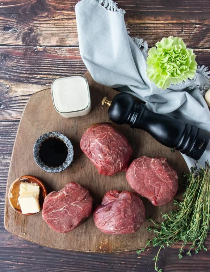 Ingredients to make steak and peppercorn steak sauce on a board including the filet mignon, cream, dijon, Worcestershire , peppercorns