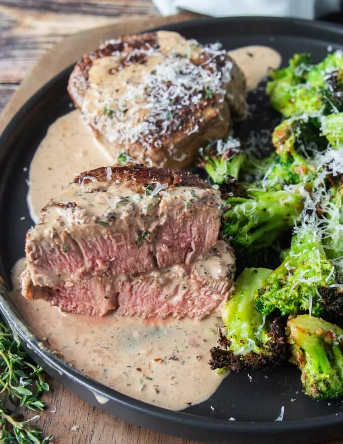 A cut up piece of tenderloin showing the pink inside and the peppercorn sauce drenching the steak