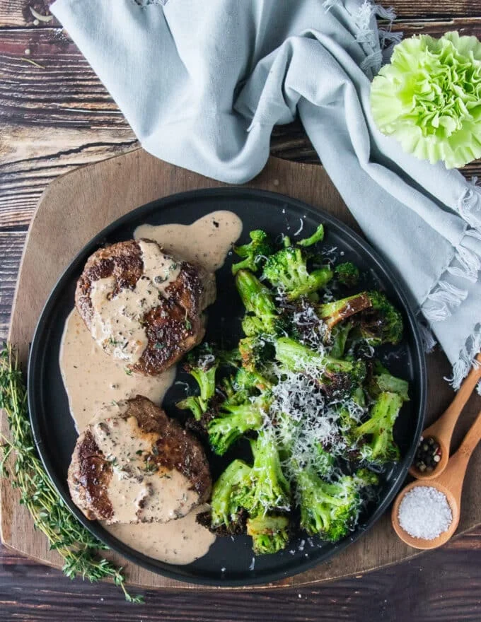 A plate of steak with peppercorn steak sauce and some air fried broccoli on the side